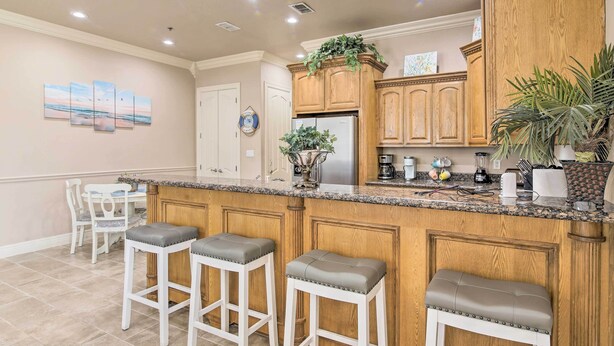 A kitchen with wooden cabinets, a granite countertop, and a built-in island with bar stools. - South Padre Island Condo - 200 Ft to Beach! (South Padre Island)
