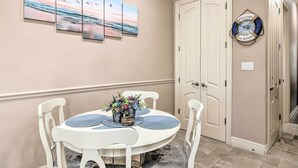 A dining area with a round table, white chairs, and a wall-mounted clock. - South Padre Island Condo - 200 Ft to Beach! (South Padre Island)