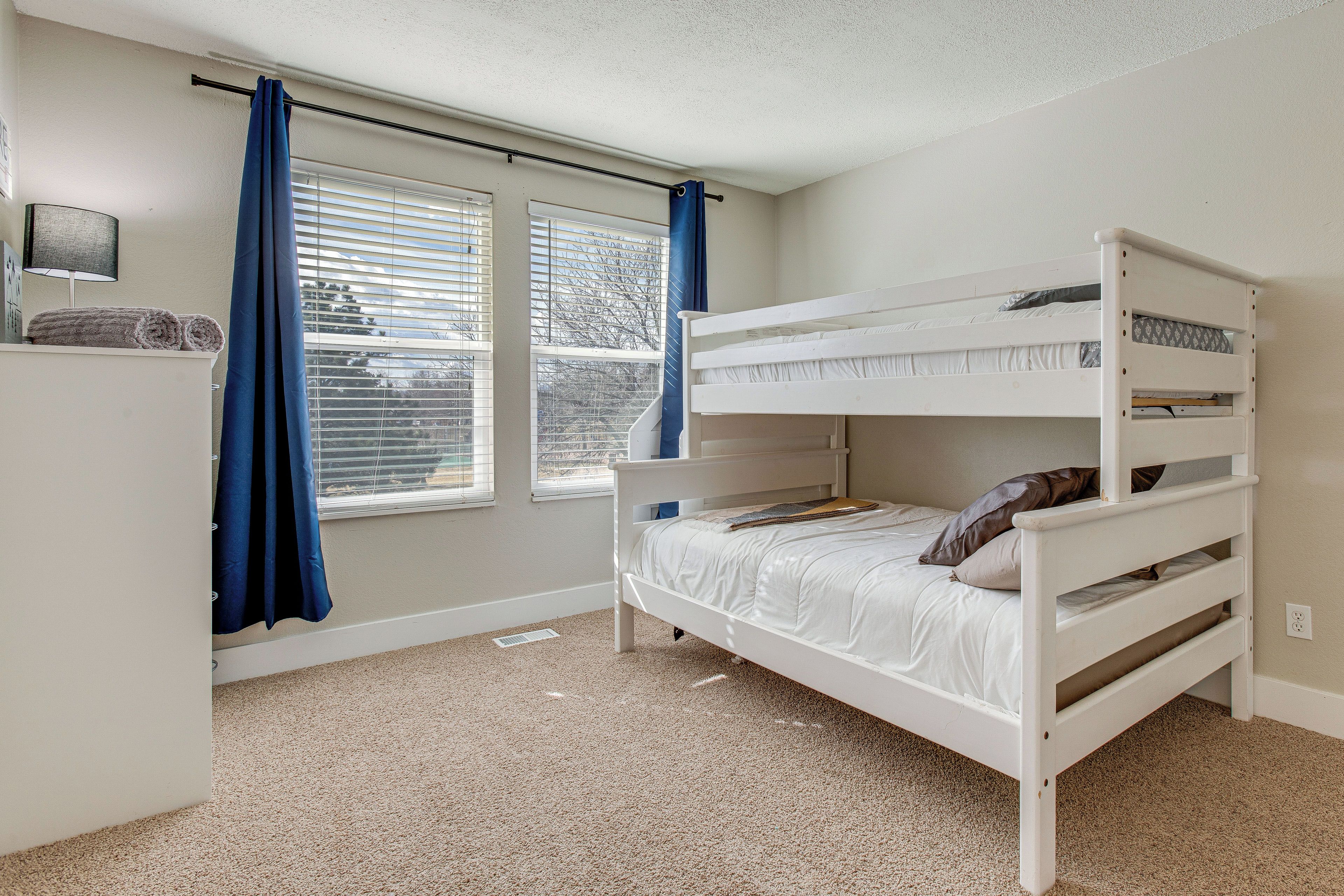 A bunk bed room with a window, curtains, and a lamp.