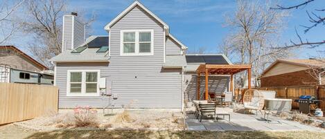 A two-story house with a covered patio area, a chimney, and a backyard with a grill and outdoor furniture.