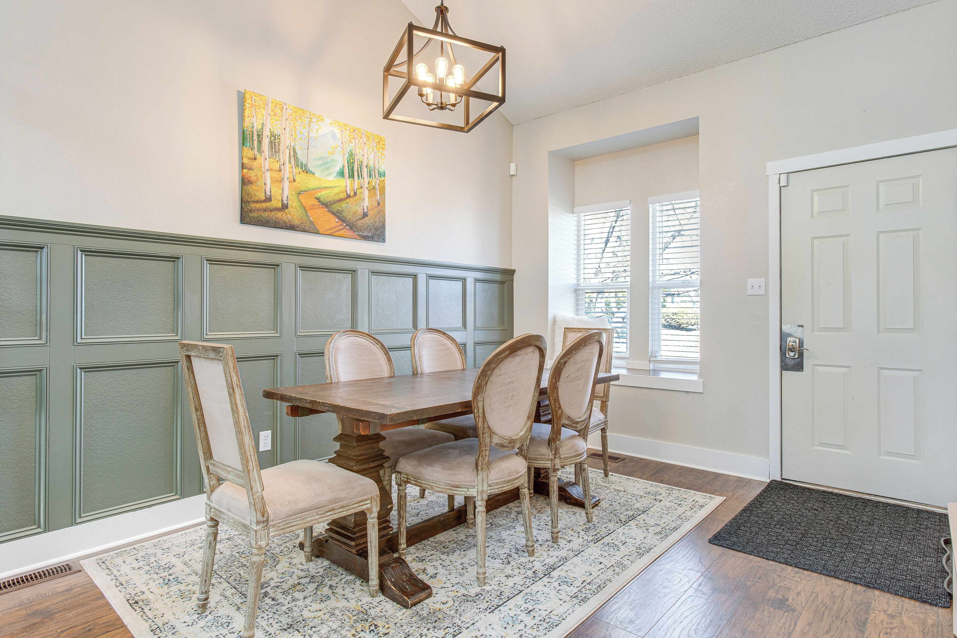 A dining area with a wooden table and chairs, a painting on the wall, and a window with blinds.