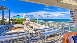 A rooftop lounge area with sun loungers, umbrellas, and a view of the ocean.