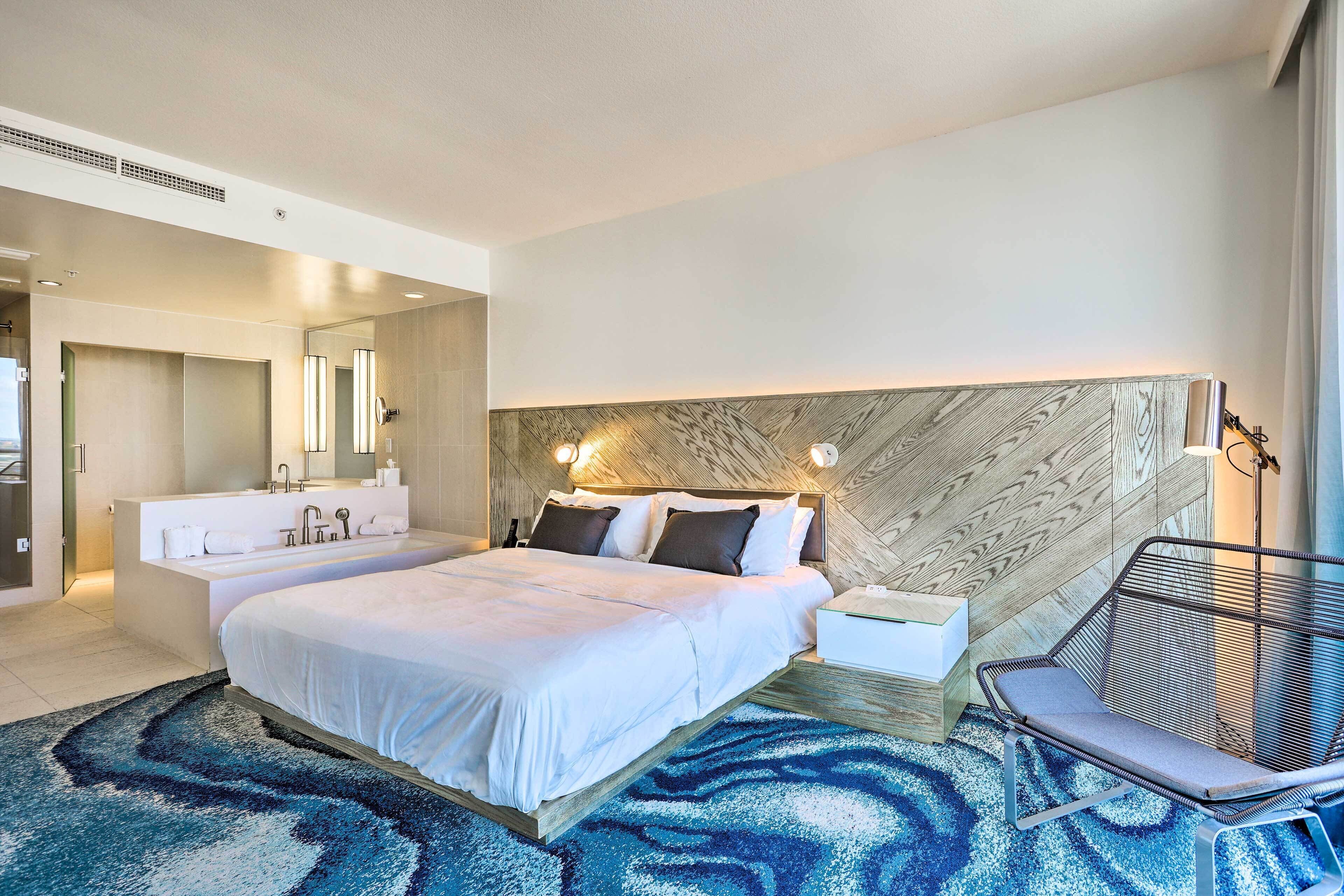 Une chambre d’hôtel moderne dotée d’un grand lit, d’une salle de bain séparée, d’un coin salon et d’une tête de lit en bois originale.