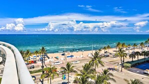 A coastal view with a beach, palm trees, and a clear blue sky.