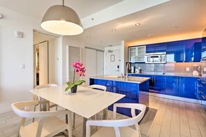 A modern kitchen with blue cabinets, a white dining table with chairs, and a pendant light.