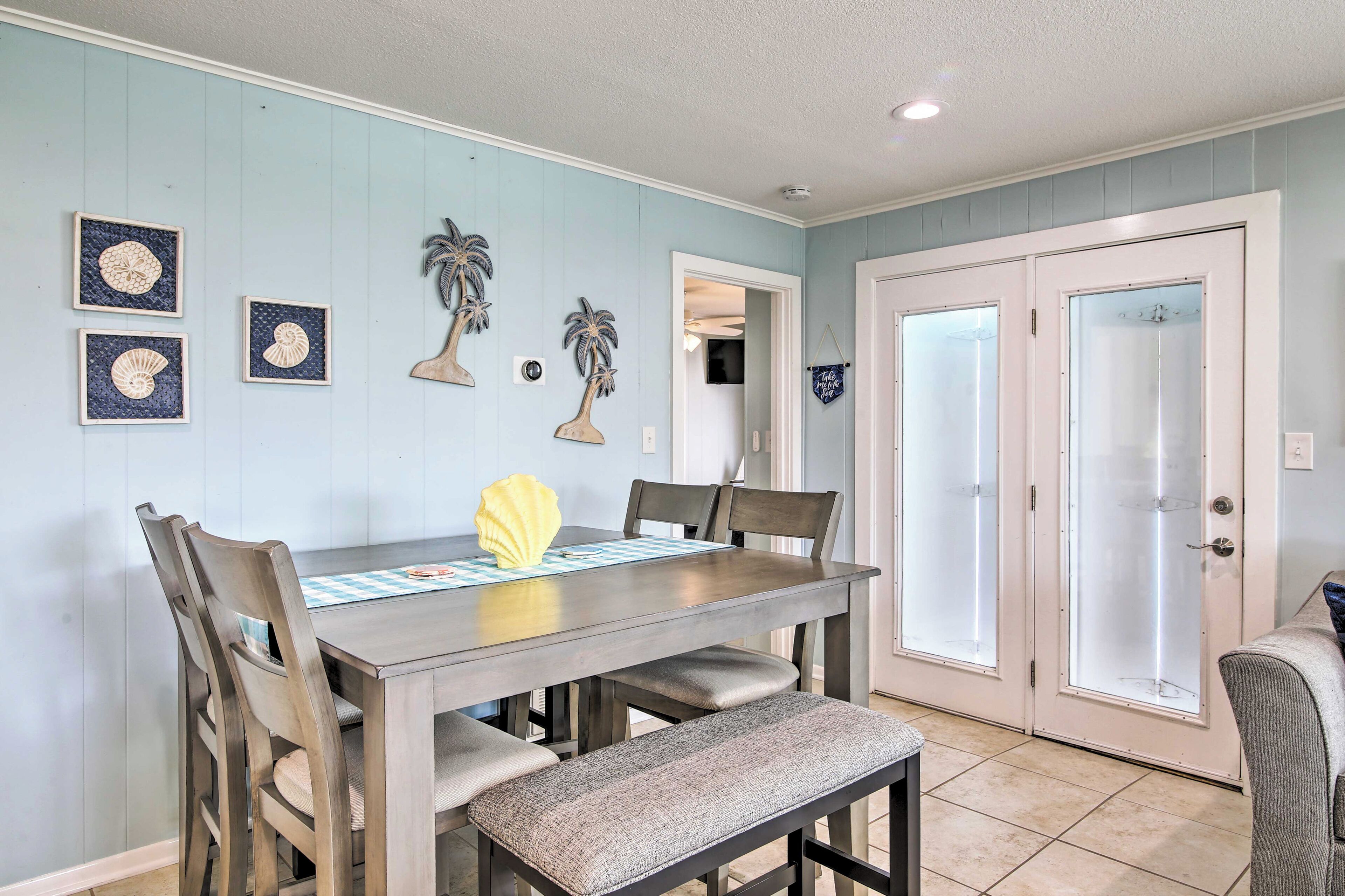 A dining area with a wooden table, chairs, and a bench. There are decorative wall art pieces and a door with frosted glass panels.