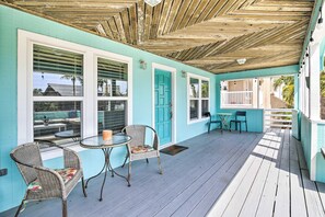 Een overdekt terras met rieten stoelen en een tafel, turquoise wanden en een houten plafond.