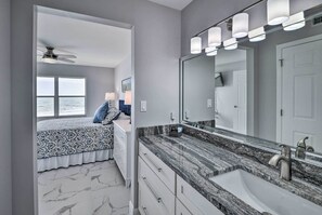 A modern bathroom with a large mirror, granite countertop, and a ceiling fan. - Oceanfront Ormond Beach Condo - Steps to Shore! (Ormond Beach)
