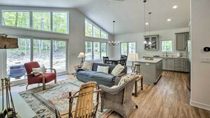 A spacious living room with a sofa, chairs, and a dining area. Large windows provide natural light and a view of the outdoors. - Door County Family Home: 3 Mi Whitefish Dunes (Sturgeon Bay)