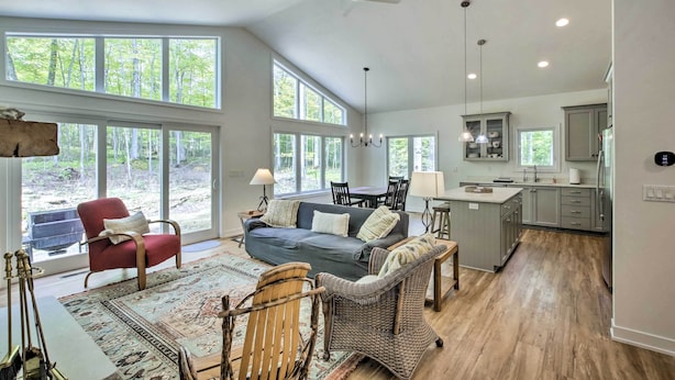 A spacious living room with a sofa, chairs, and a dining area. Large windows provide natural light and a view of the outdoors. - Door County Family Home: 3 Mi Whitefish Dunes (Sturgeon Bay)