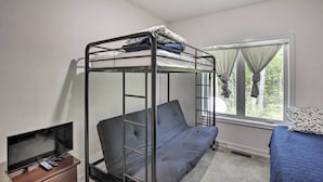 A bunk bed with a TV on a wooden side table, a window with curtains, and a bed with a blue quilt. - Door County Family Home: 3 Mi Whitefish Dunes (Sturgeon Bay)
