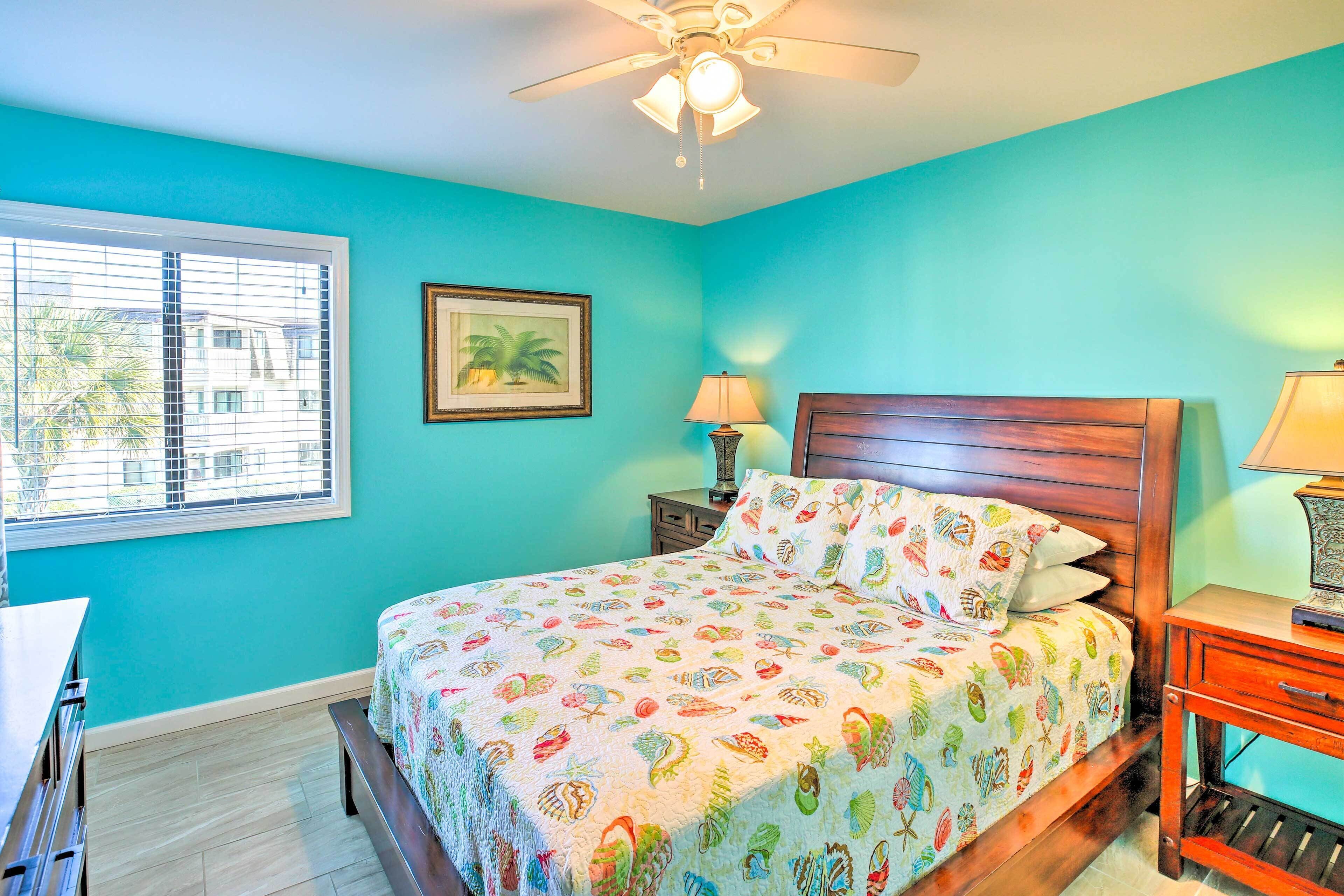 A bedroom with a bed, wooden headboard, two bedside tables with lamps, a window with blinds, and a ceiling fan.