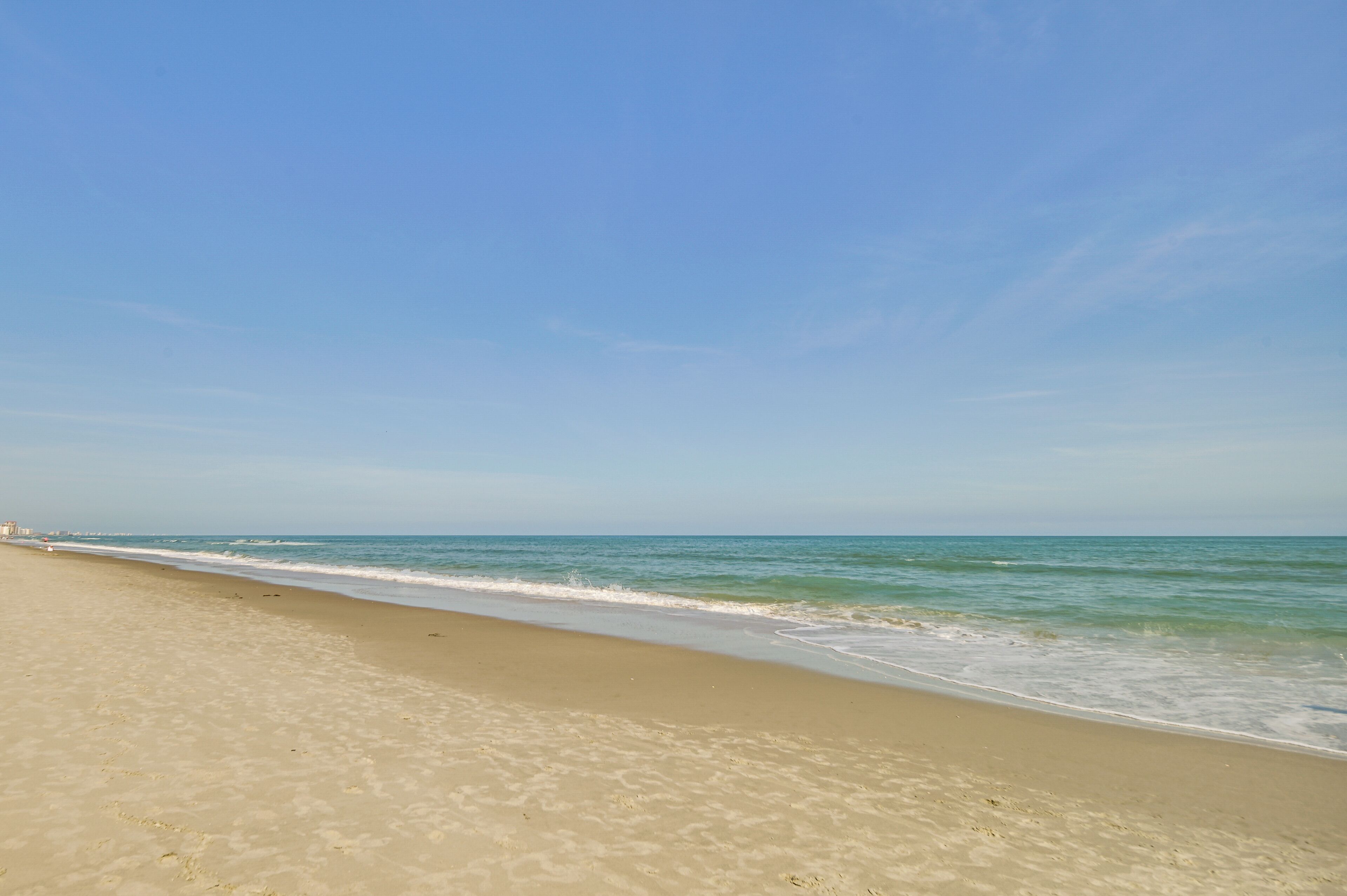 Ampia spiaggia sabbiosa con onde calme e cielo sereno.