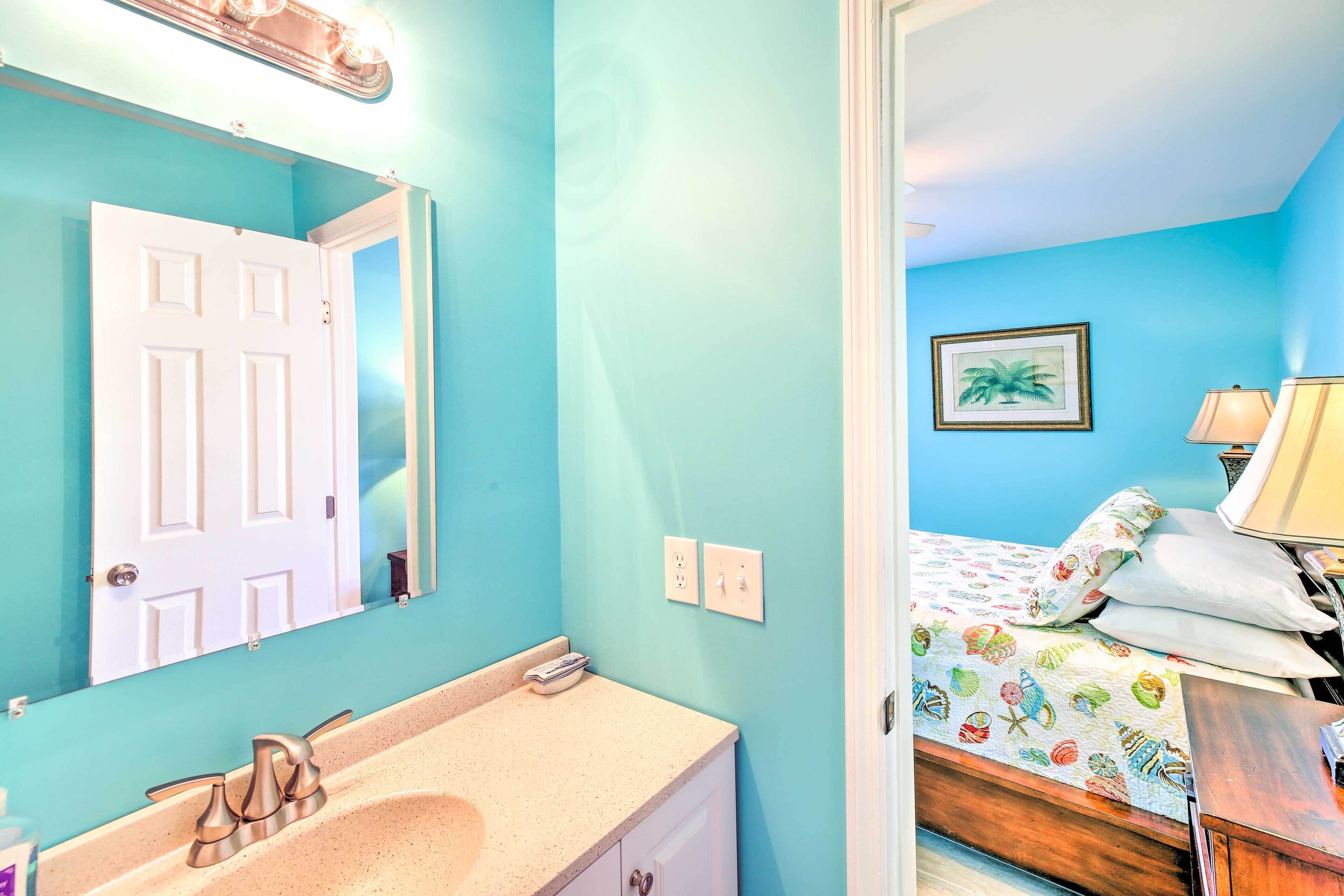 A bathroom with a sink, mirror, and a door leading to a bedroom with a bed and a nightstand.