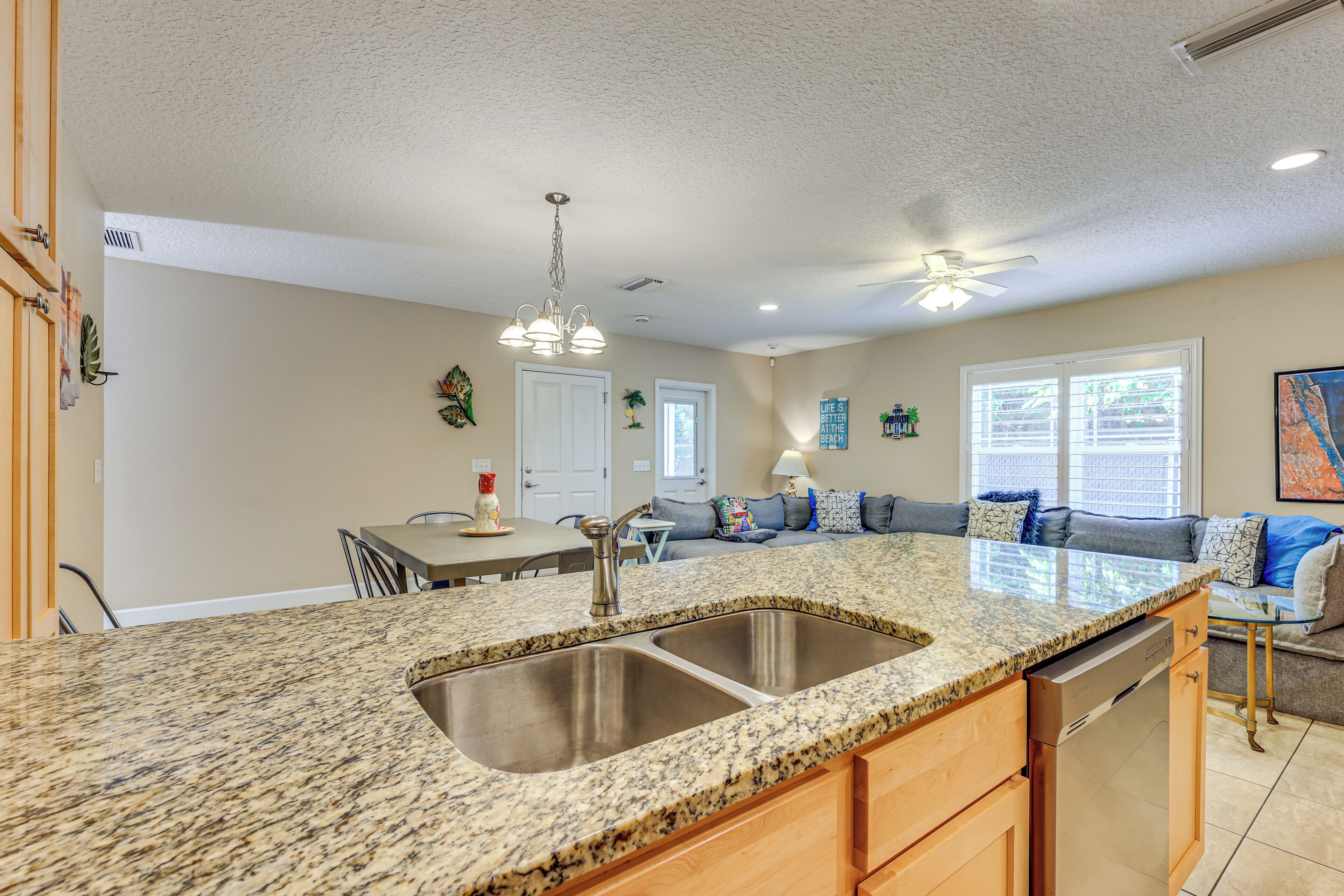 A kitchen with granite countertops, stainless steel sink, and wooden cabinets. There is a dining area with a table and chairs.