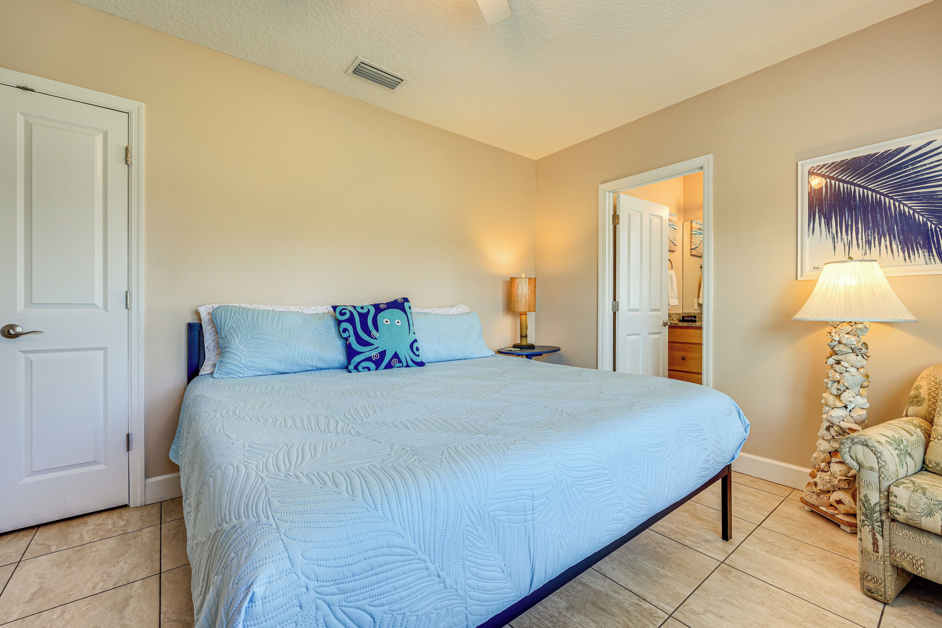 A bedroom with a large bed, a nightstand, a lamp, and a chair.