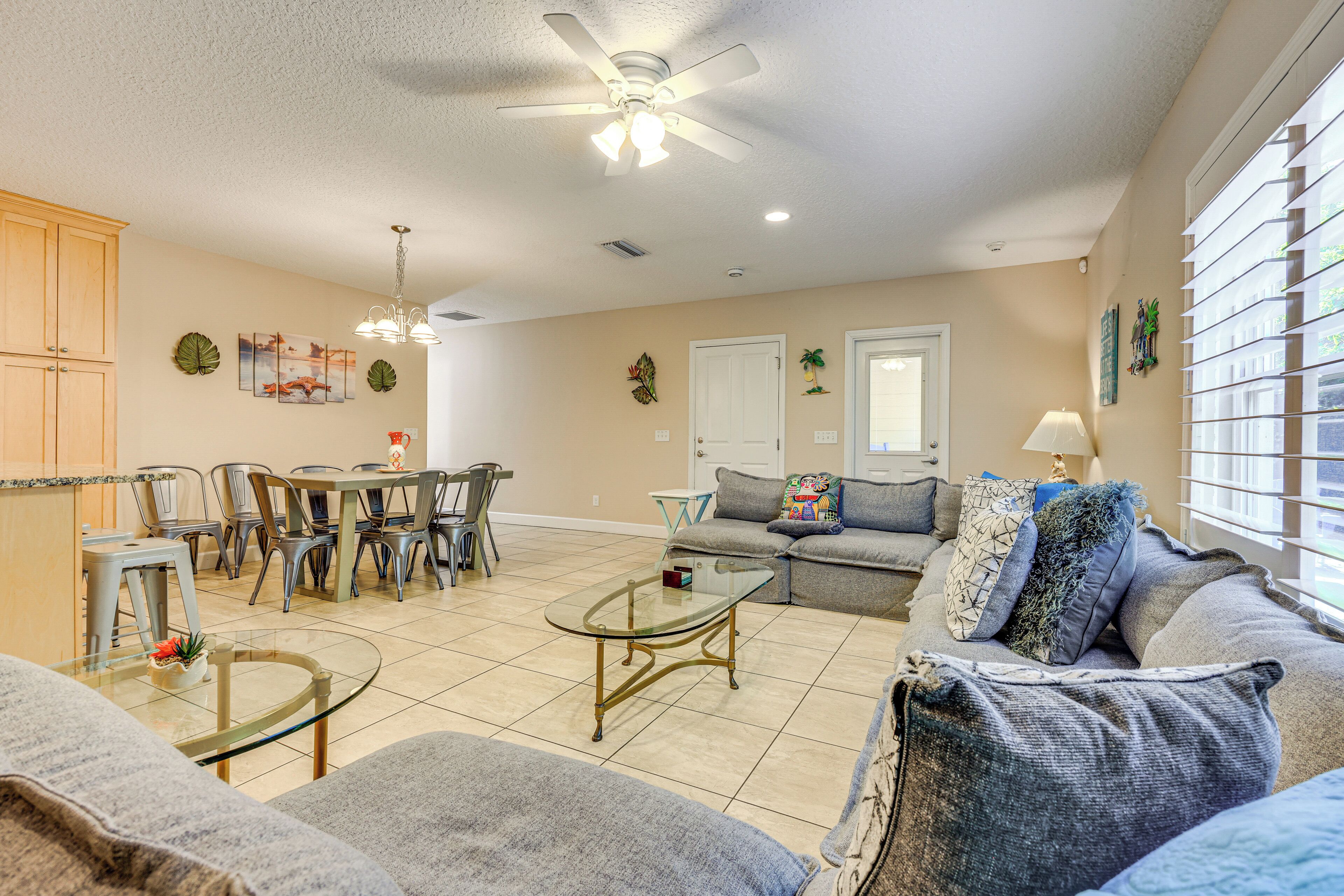 A spacious living room with a dining area, a ceiling fan, and a large window with blinds.