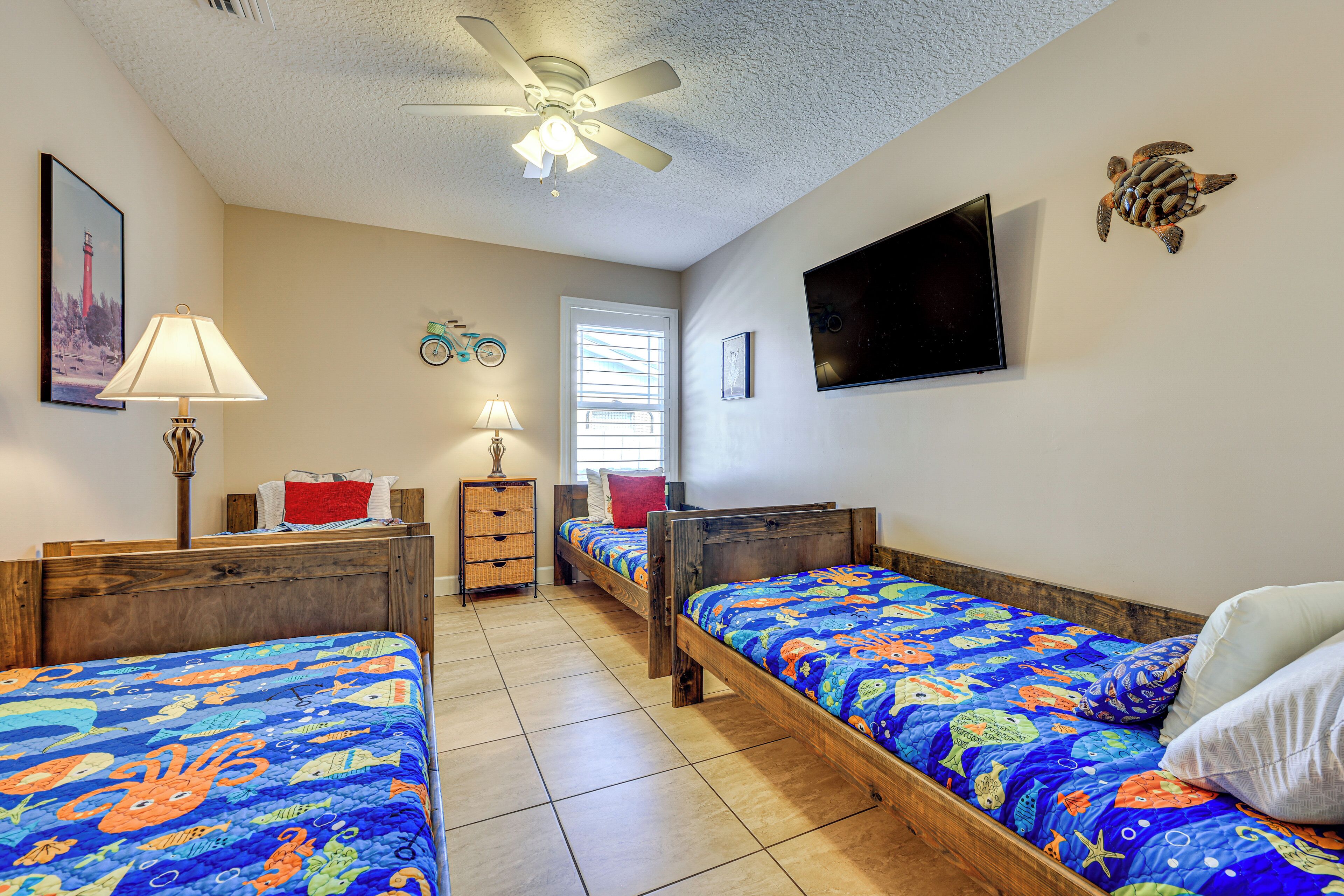 A bedroom with two wooden beds, a ceiling fan, a TV, and a window with blinds.