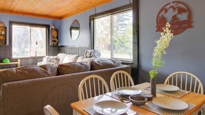 A cozy dining area with a wooden table set for two, a cushioned bench, and a large window providing natural light. - Quaint Ironton Getaway w/ Fire Pit, Gas Grill! (Ironton)