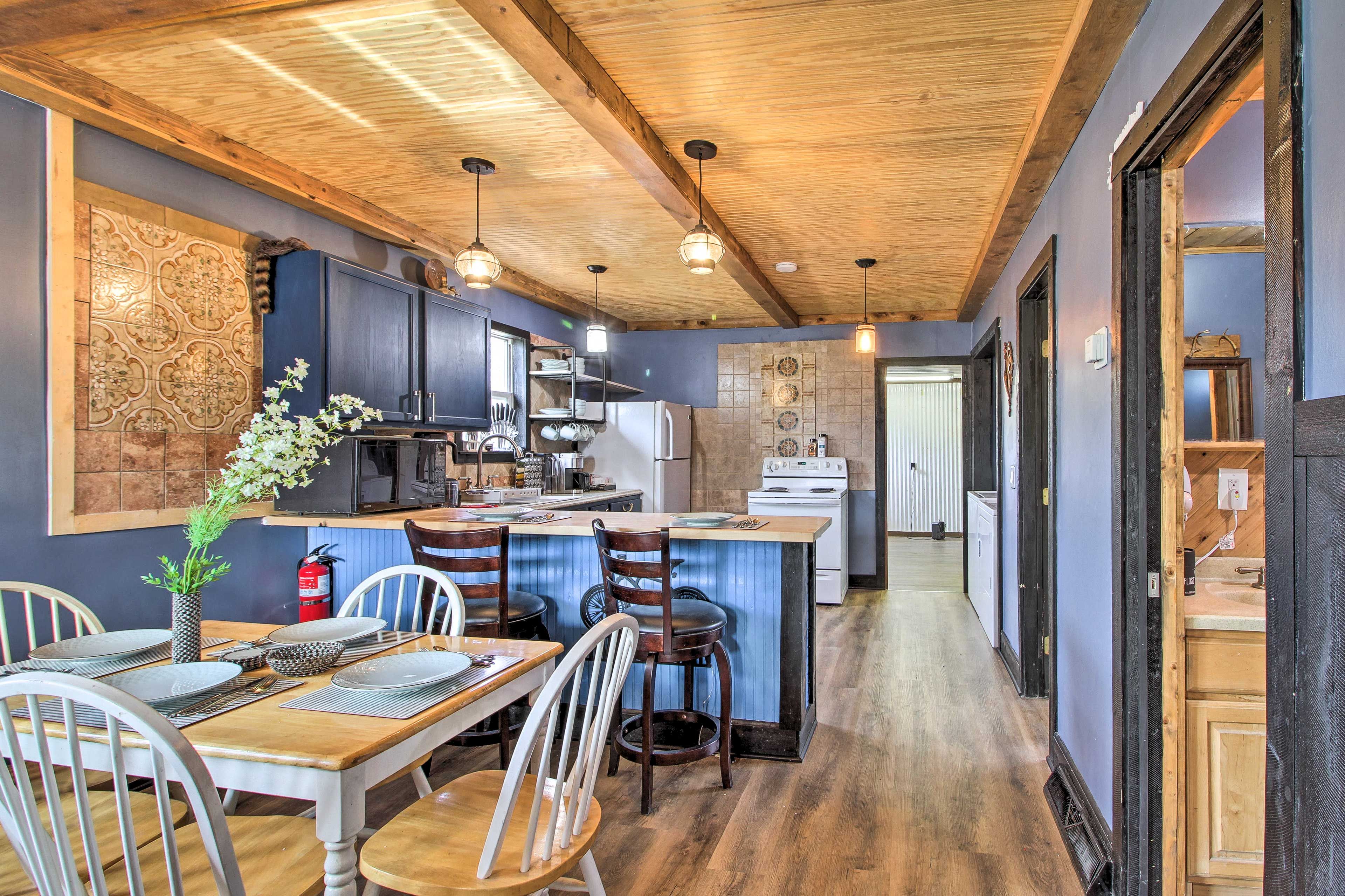 Una cocina moderna con vigas de madera en el techo, una isla central y un comedor con sillas blancas y una mesa de madera.