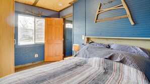A bedroom with a wooden ceiling, a bed with a striped blanket, a wooden ladder on the wall, and a window with a view of trees. - Quaint Ironton Getaway w/ Fire Pit, Gas Grill! (Ironton)