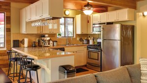 A kitchen with wooden cabinets, a stainless steel refrigerator, a stove, and a ceiling fan. - Spacious Groveland Cabin w/ Wraparound Deck! (Groveland)