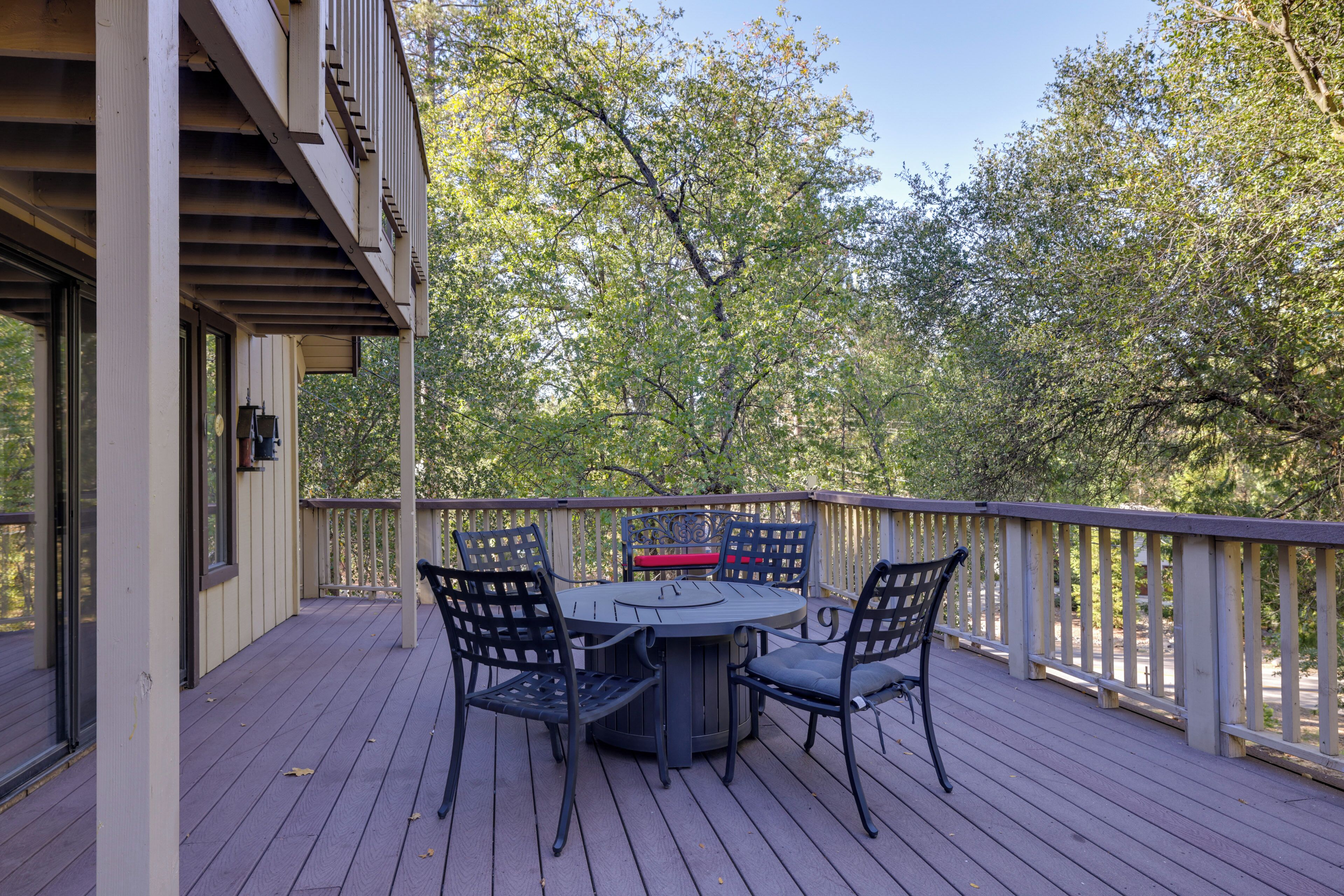 Une terrasse en bois avec une table ronde et quatre chaises, entourée d’une balustrade blanche.