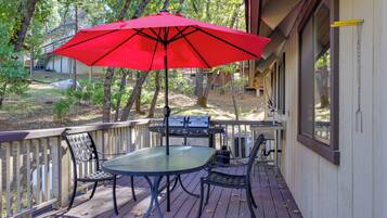 A deck with a table and chairs, a red umbrella, and a grill.