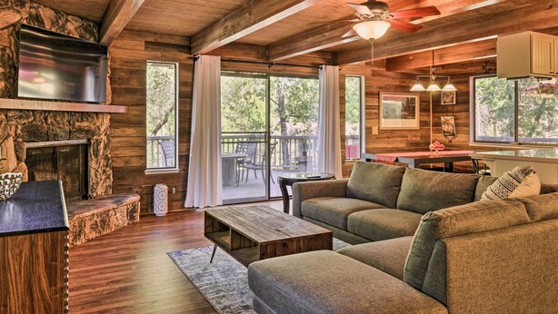 A cozy cabin interior with a stone fireplace, wooden ceiling beams, a sofa, and a dining area with a view of the outdoors. - Spacious Groveland Cabin w/ Wraparound Deck! (Groveland)