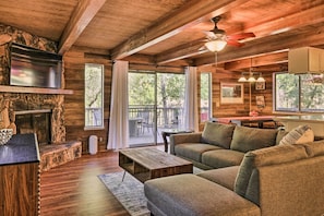 A cozy cabin interior with a stone fireplace, wooden floors, a sofa, and a dining area.