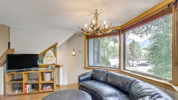 A living room with a large window, a leather sofa, a television on a wooden stand, and a chandelier. - Telluride Condo: Walk to Lift, Bear Creek, & More! (Telluride)
