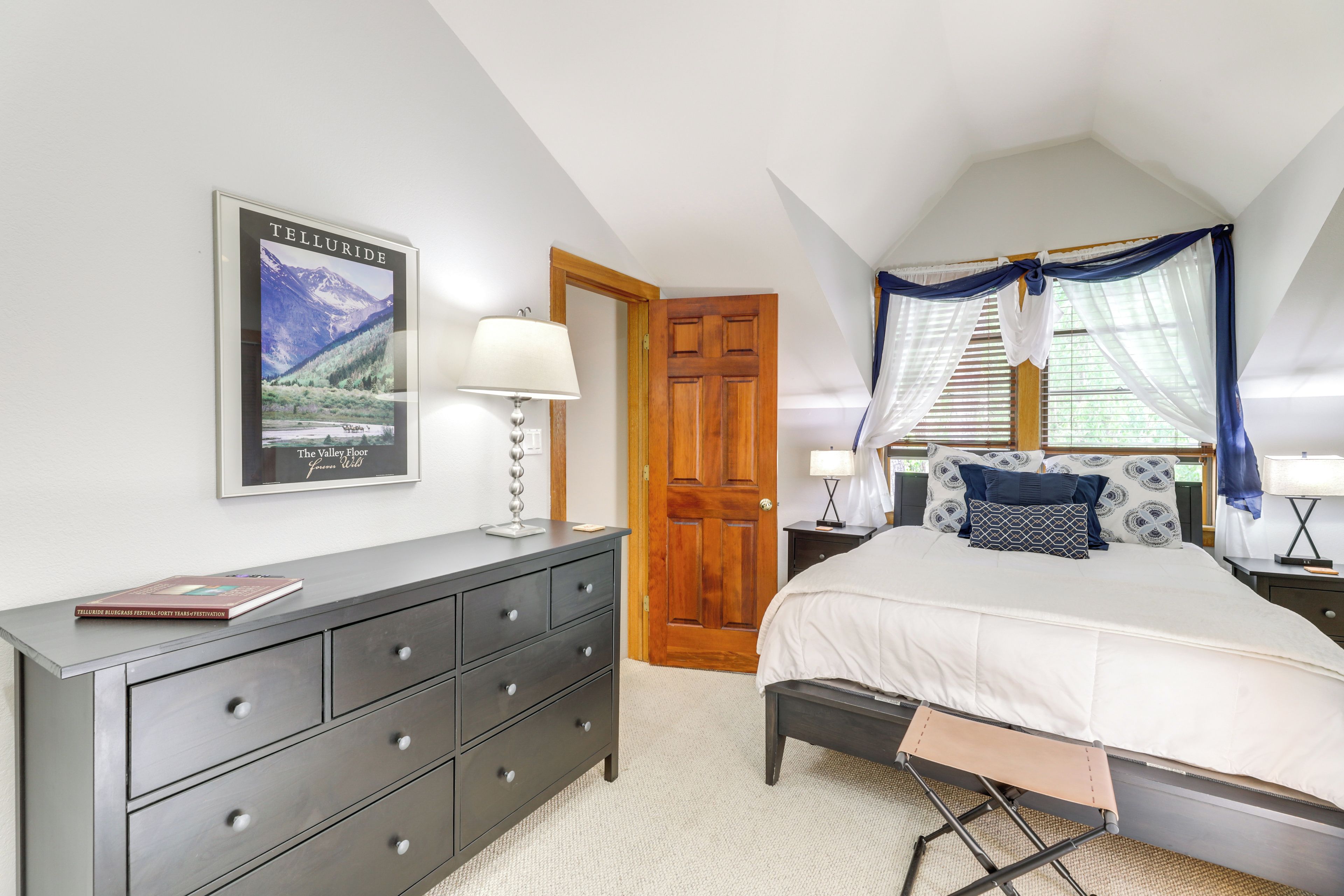 A bedroom with a bed, a dresser, a door, and a window with curtains.