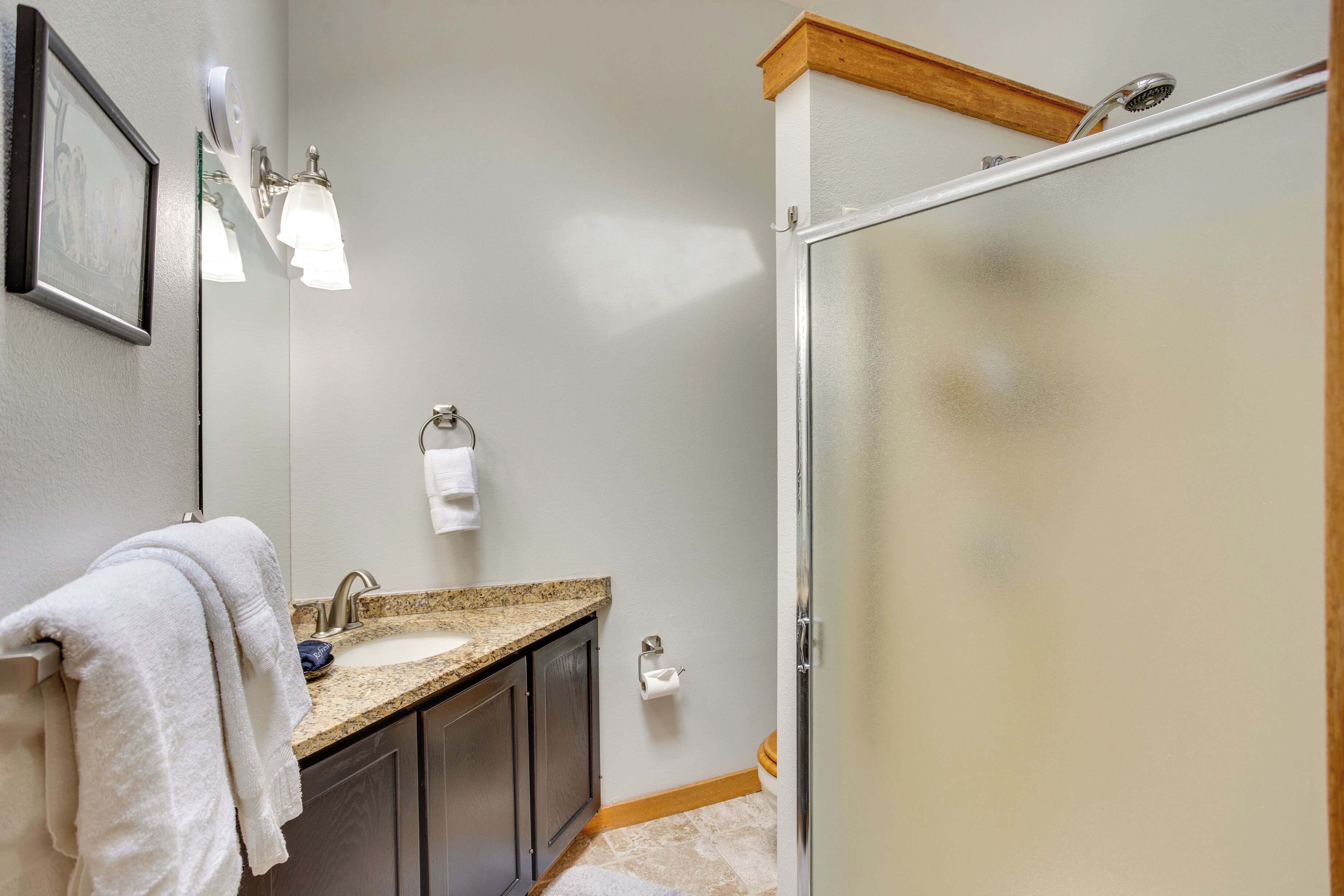 A bathroom with a granite countertop sink, a mirror, a towel rack, and a glass shower enclosure.