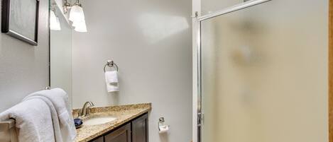 A bathroom with a granite countertop sink, a mirror, a towel rack, and a glass shower enclosure.