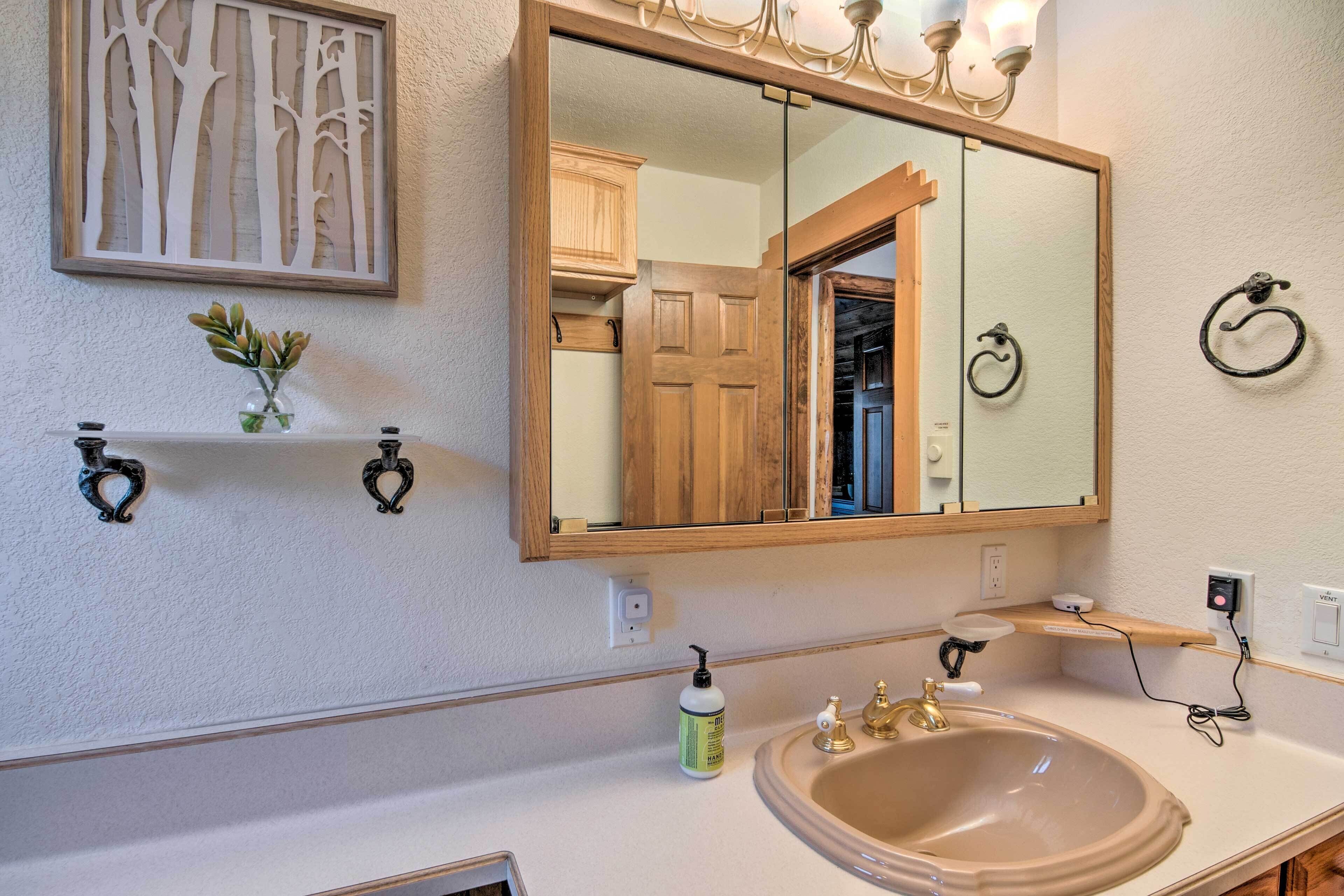 Une salle de bain avec un grand miroir, des meubles en bois, un lavabo et une petite étagère sur laquelle est posé un vase.