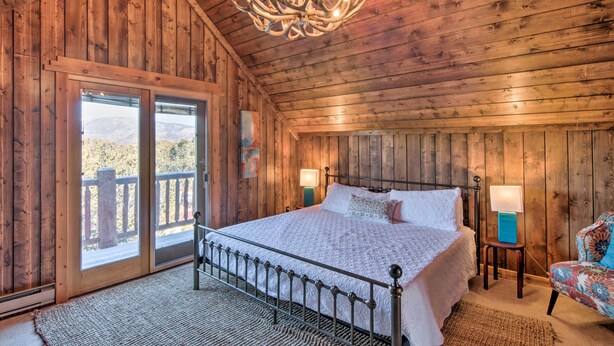 A wooden cabin bedroom with a bed, two bedside lamps, a chandelier, and a view through a sliding door. - Buena Vista Oasis w/ Mtn Views, 3 Mi to Dtwn! (Buena Vista)