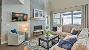 A modern living room with a fireplace, a sofa, a coffee table, and a TV mounted on the wall. - Granby Golf Retreat w/ Ski Trails, Mountain View! (Granby)