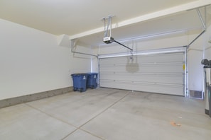 Uma garagem com porta fechada, projetor fixado no teto e duas lixeiras azuis.