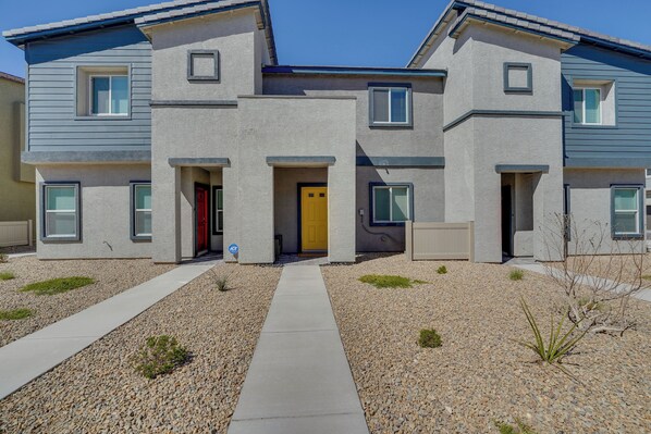 A modern two-story residential building with a central entrance, a gravel driveway, and a small garden area.