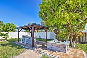 Een achtertuin met een houten pergola, een barbecueplaats met stenen en een boom.