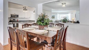 A dining area with a wooden table set for six, surrounded by wooden chairs. A large potted plant is on the table, and the room has white walls and hardwood flooring. - Centennial Home w/ Game Room, 11 Mi to Downtown! (Littleton)