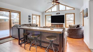 A spacious living area with a high ceiling, a central bar with stools, a large flat-screen TV, and a cozy seating area with a fireplace. - Centennial Home w/ Game Room, 11 Mi to Downtown! (Littleton)