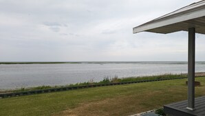 Une vue sur une étendue d’eau, avec une zone herbeuse au premier plan et une structure couverte sur la droite.