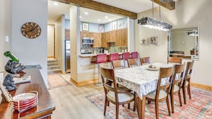 A dining area with a wooden table and chairs, a kitchen in the background, and a clock on the wall. - Newly Upgraded Avon Condo w/ Pool & Hot Tub Access (Avon)