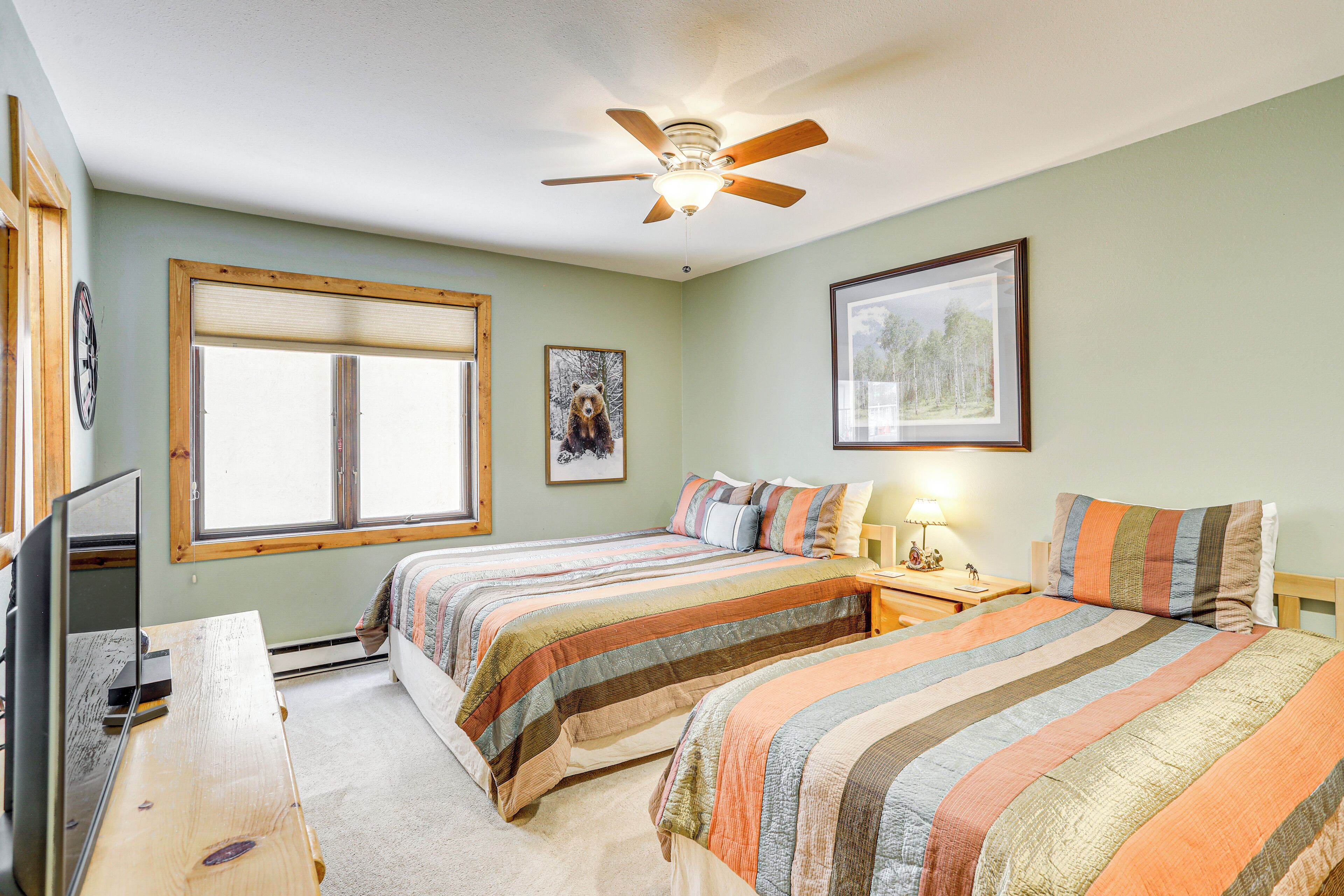 A bedroom with two beds, a ceiling fan, a window, and a TV.