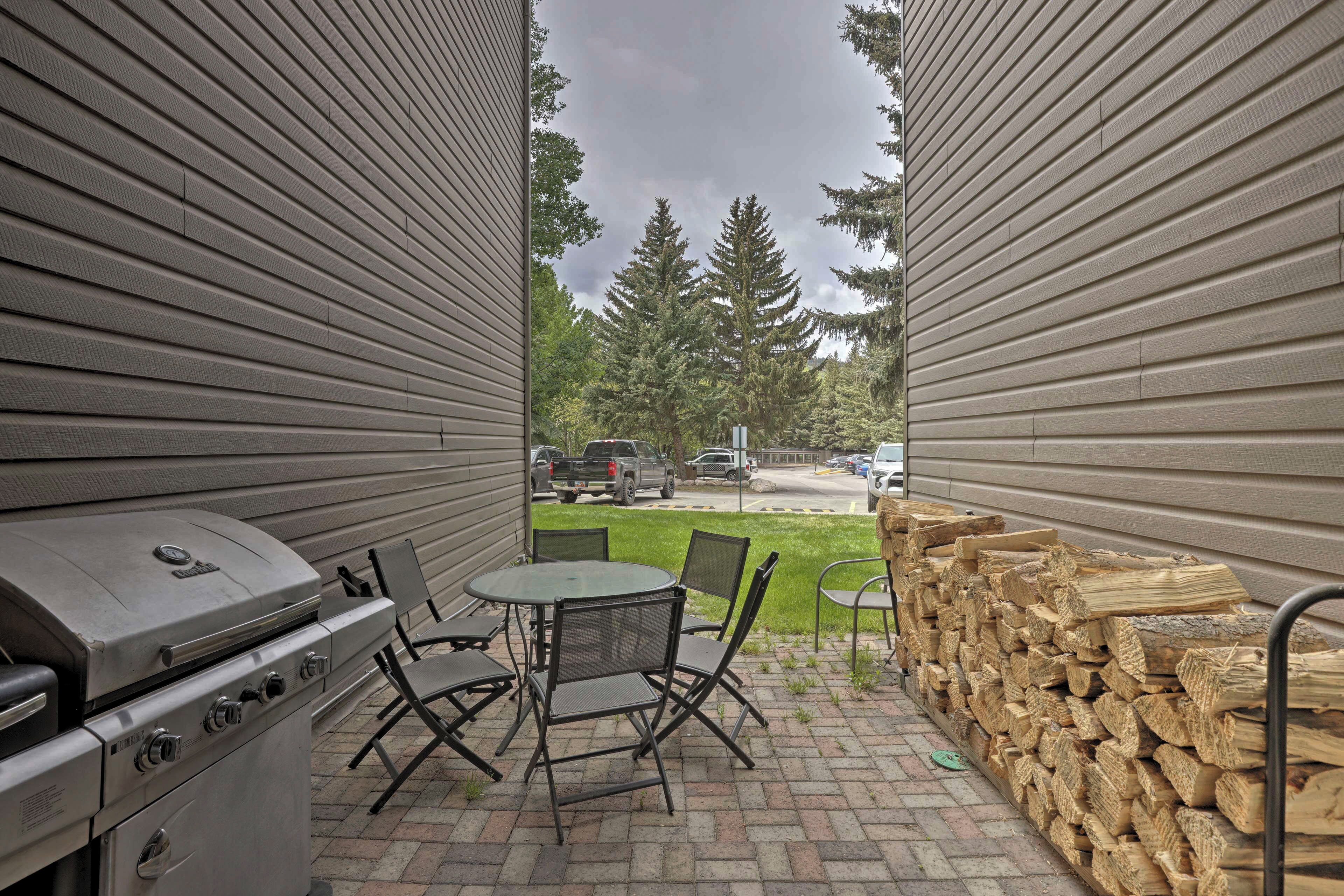 Une terrasse avec un barbecue, des chaises pliantes et une pile de bois de chauffage.