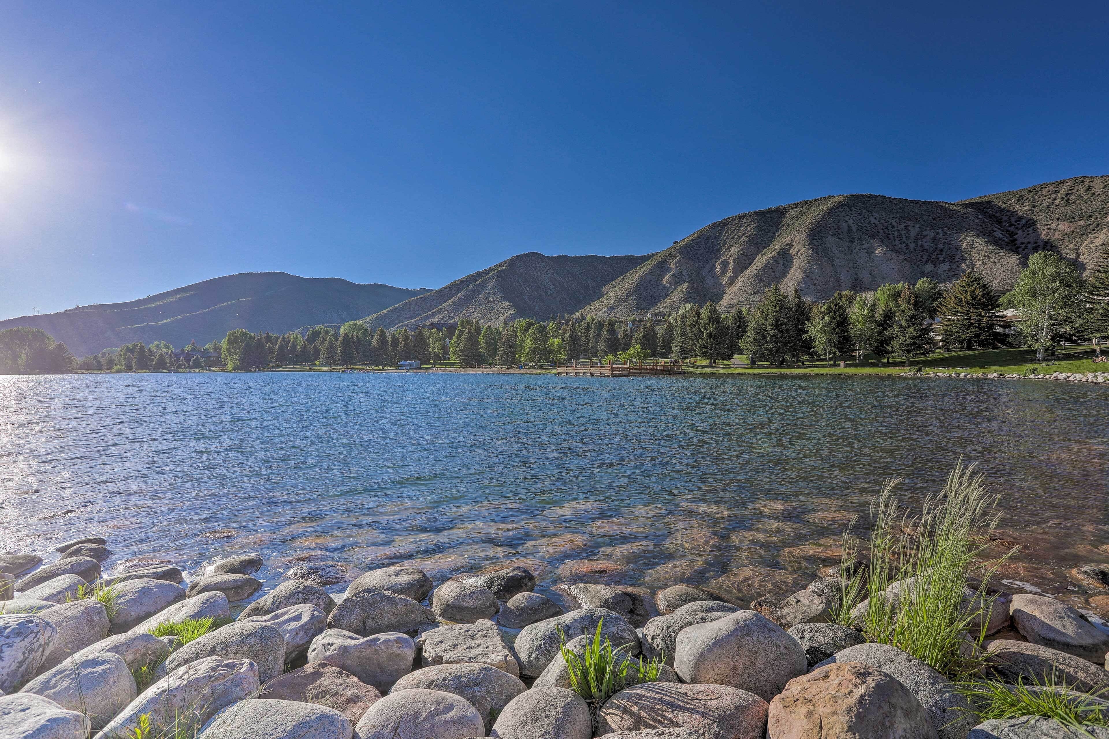 A lake with clear water, surrounded by large rocks and trees, and mountains in the background.