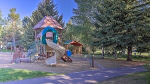 A playground with a slide and climbing structures, surrounded by trees and a covered playhouse. - Newly Upgraded Avon Condo w/ Pool & Hot Tub Access (Avon)
