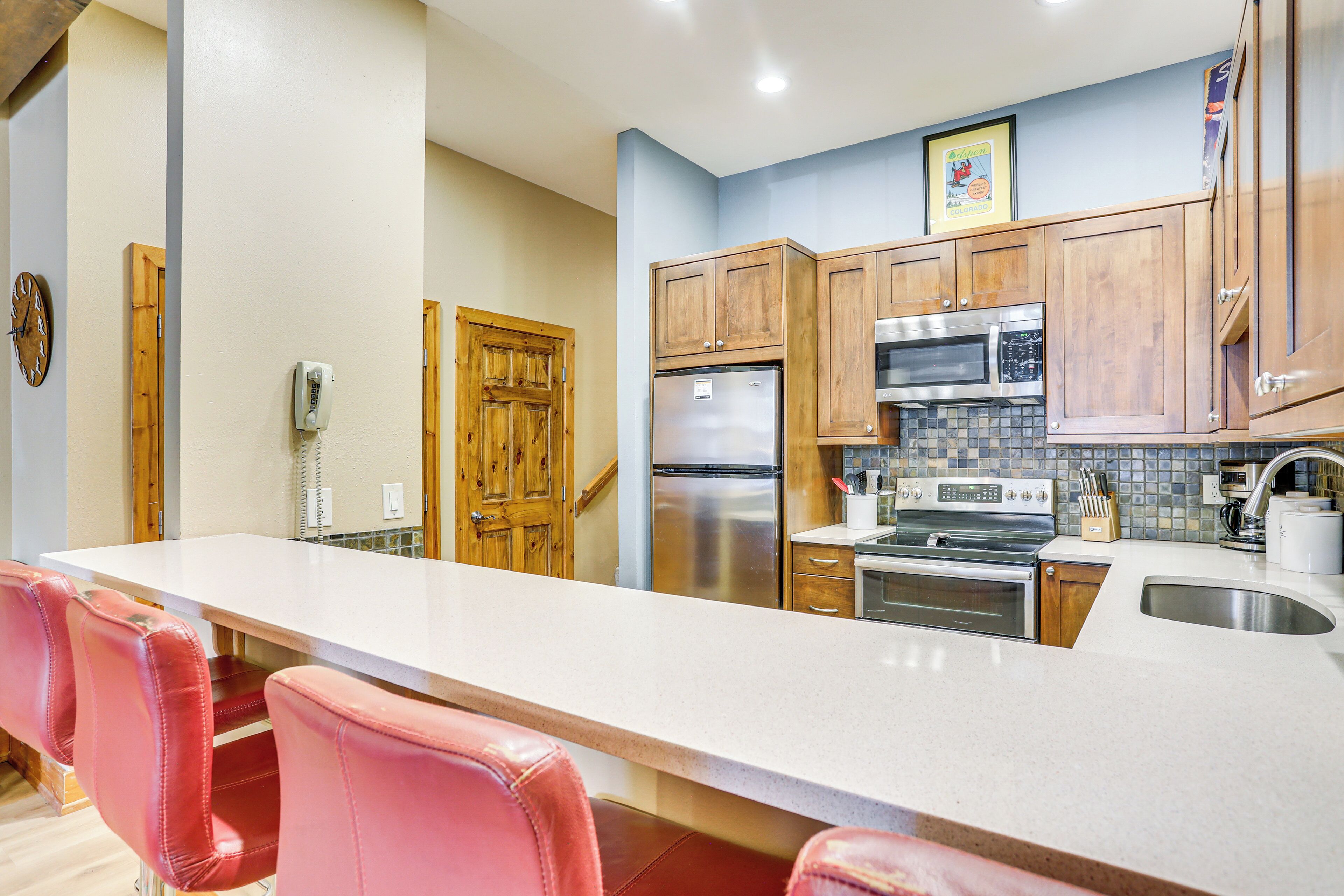 A kitchen with wooden cabinets, stainless steel appliances, a white countertop, and red bar stools.