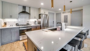 Une cuisine moderne avec des meubles gris, des appareils en acier inoxydable, un îlot en marbre et des luminaires suspendus.